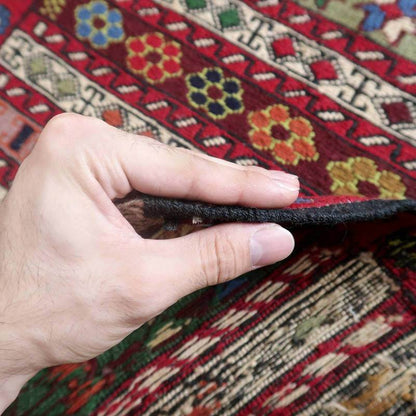 Hand holding edge of detailed multi-colored wool Kilim rug from Azerbaijan, showcasing thick, high-quality smac weaving technique.